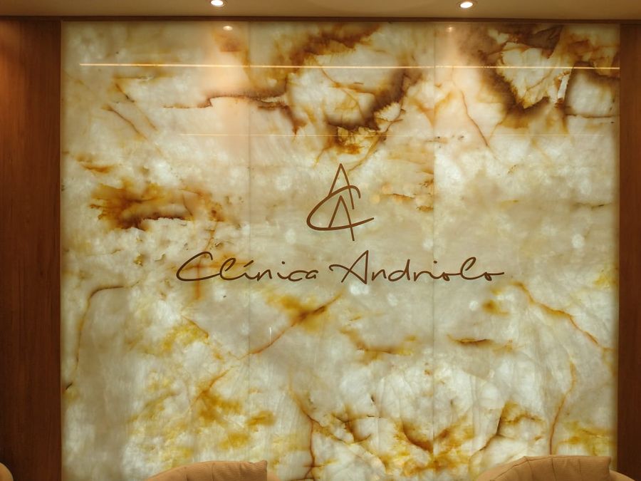 Logotipo Clínica Andriolo em dourado sobre painel de ônix retroiluminado