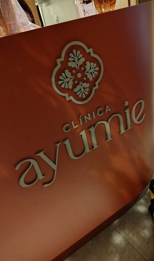 Logotipo Clínica Ayumie em acrílico dourado sobre balcão terracota
